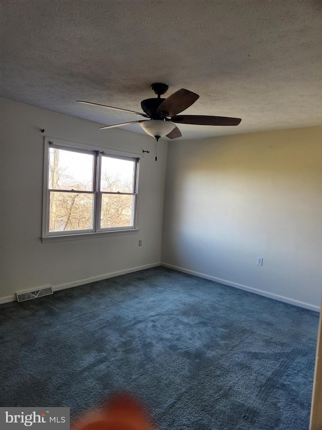 unfurnished room with ceiling fan, dark carpet, and a textured ceiling