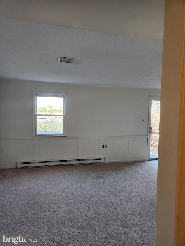 carpeted empty room with a baseboard heating unit