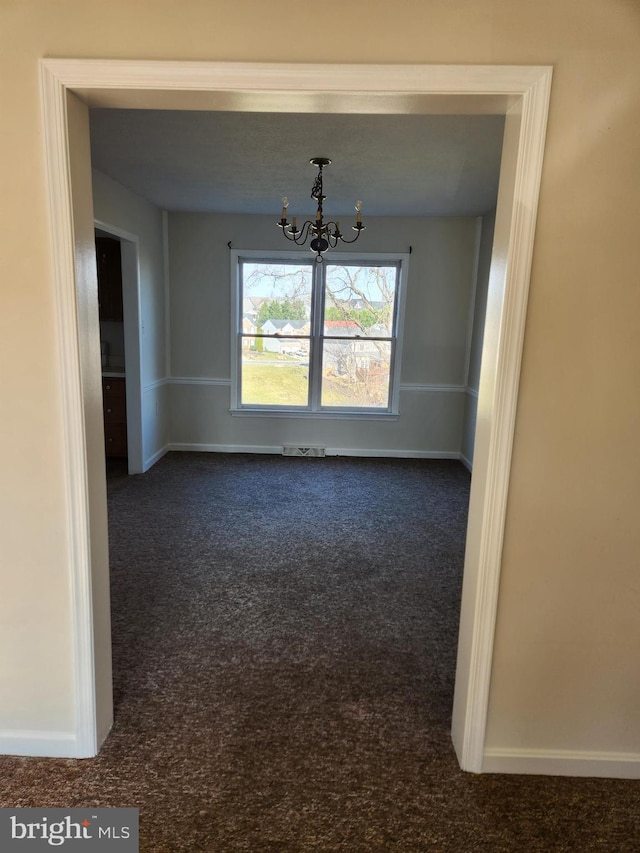 empty room with dark colored carpet and an inviting chandelier