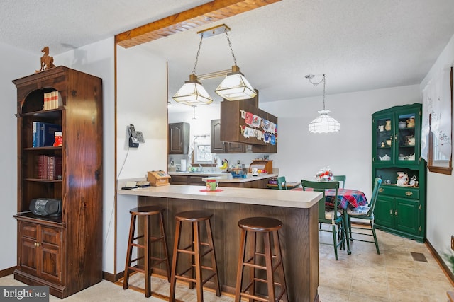 kitchen featuring a breakfast bar, dark brown cabinetry, kitchen peninsula, and a textured ceiling