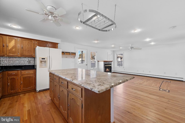 kitchen featuring decorative backsplash, light wood-type flooring, a baseboard heating unit, white refrigerator with ice dispenser, and a kitchen island