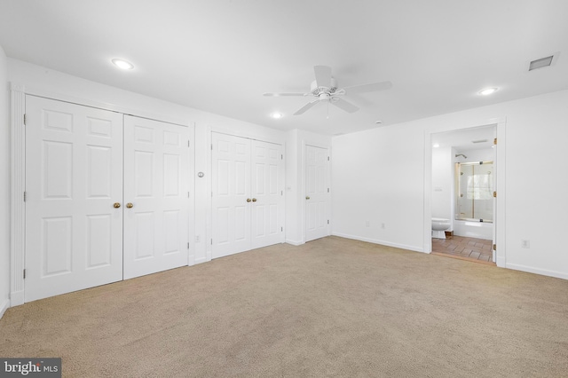 unfurnished bedroom with light colored carpet, ensuite bath, ceiling fan, and multiple closets