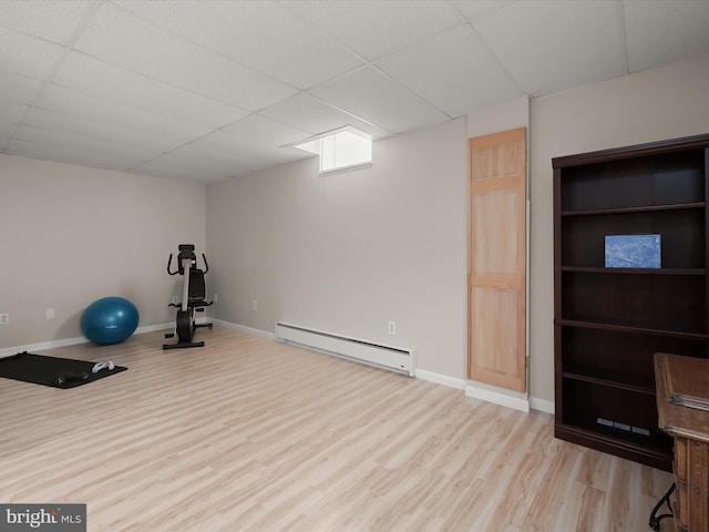 exercise area featuring a drop ceiling, a baseboard heating unit, and light wood-type flooring