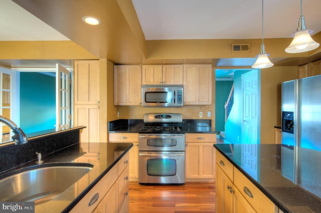 kitchen with dark stone counters, hanging light fixtures, sink, dark hardwood / wood-style floors, and appliances with stainless steel finishes