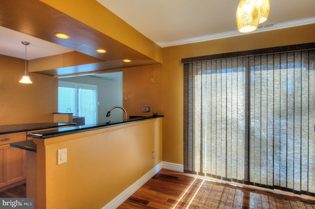 kitchen with kitchen peninsula, decorative light fixtures, dark wood-type flooring, and sink