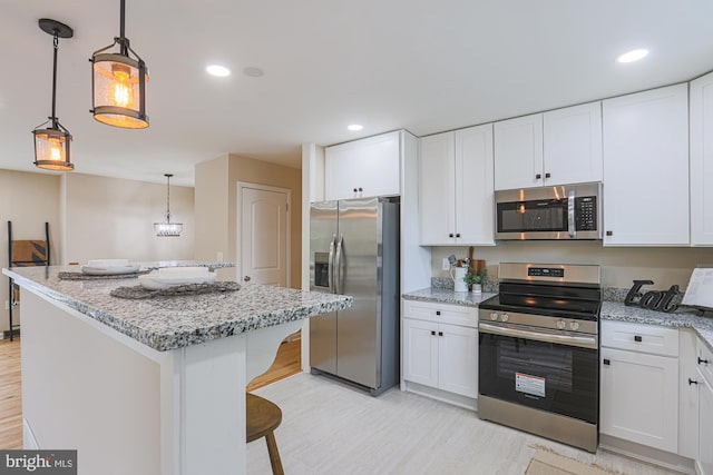 kitchen featuring light stone countertops, appliances with stainless steel finishes, decorative light fixtures, white cabinetry, and a breakfast bar area