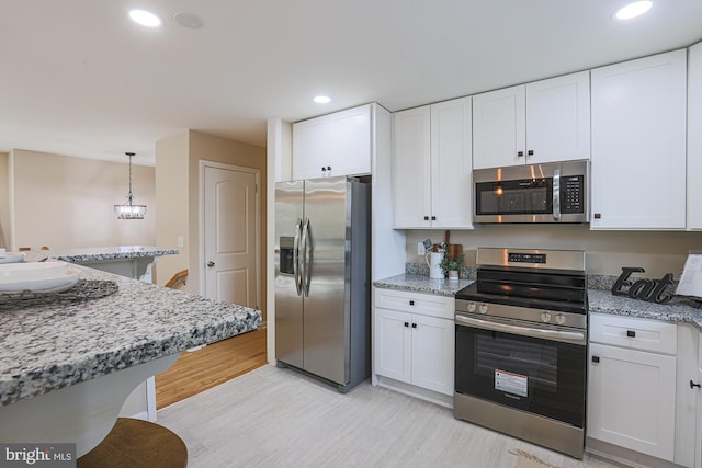 kitchen featuring light stone counters, white cabinetry, hanging light fixtures, and appliances with stainless steel finishes