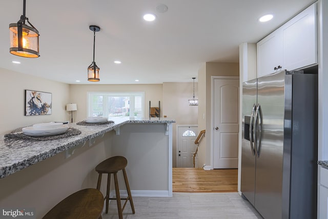 kitchen with a kitchen bar, light stone countertops, white cabinets, stainless steel fridge with ice dispenser, and hanging light fixtures