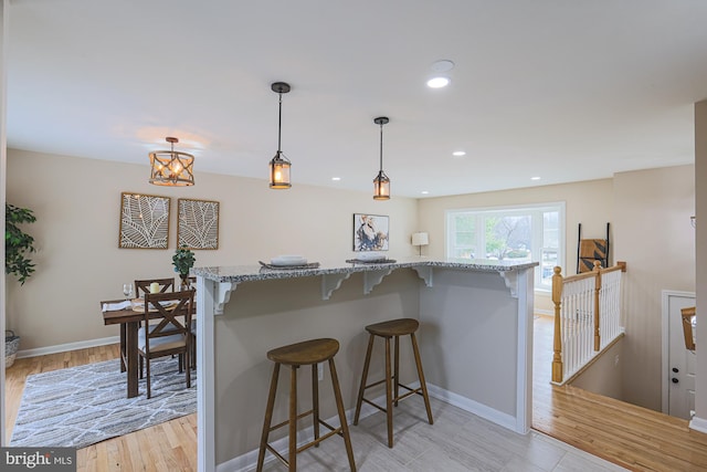 kitchen featuring a kitchen breakfast bar, light stone countertops, pendant lighting, and light wood-type flooring