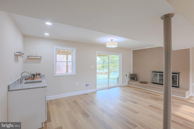 living room featuring light hardwood / wood-style flooring, sink, a fireplace, and decorative columns