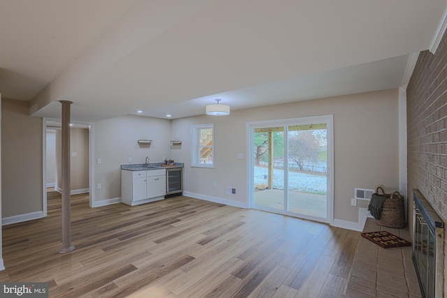 unfurnished living room featuring indoor wet bar, light wood-type flooring, beverage cooler, and a brick fireplace