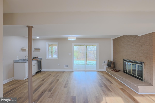 unfurnished living room with ornate columns, sink, wine cooler, light hardwood / wood-style floors, and a fireplace