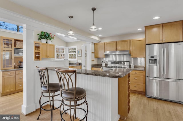 kitchen with appliances with stainless steel finishes, dark stone countertops, light hardwood / wood-style floors, a kitchen island, and decorative light fixtures