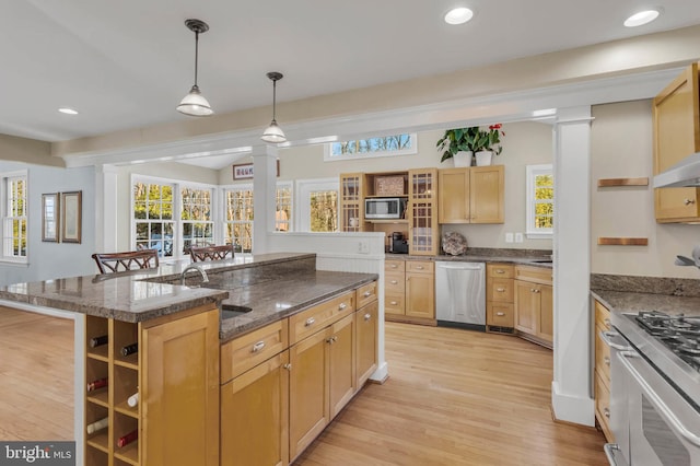 kitchen with sink, a kitchen island with sink, stainless steel appliances, a kitchen bar, and decorative light fixtures