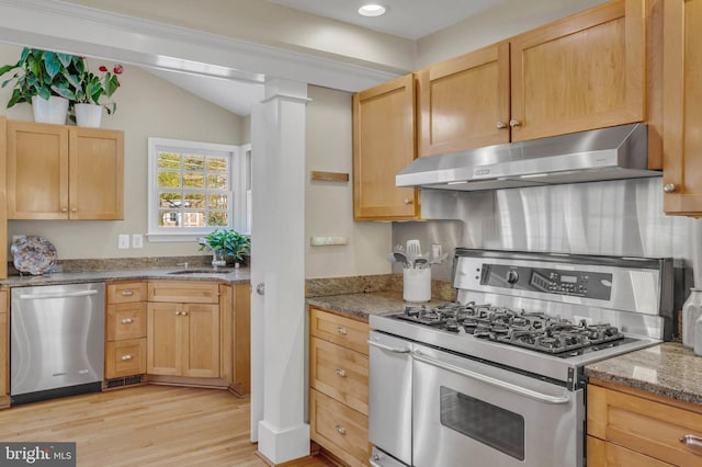 kitchen with appliances with stainless steel finishes, sink, dark stone countertops, light brown cabinets, and light wood-type flooring