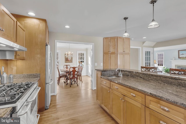 kitchen with sink, appliances with stainless steel finishes, dark stone countertops, hanging light fixtures, and light wood-type flooring