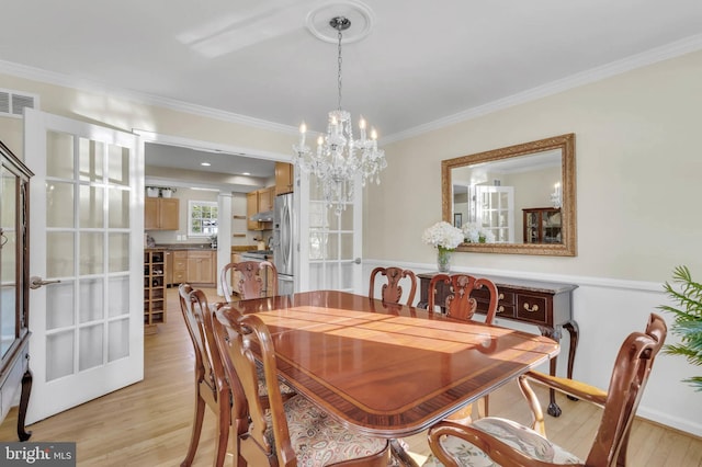 dining area featuring french doors, ornamental molding, a chandelier, and light wood-type flooring