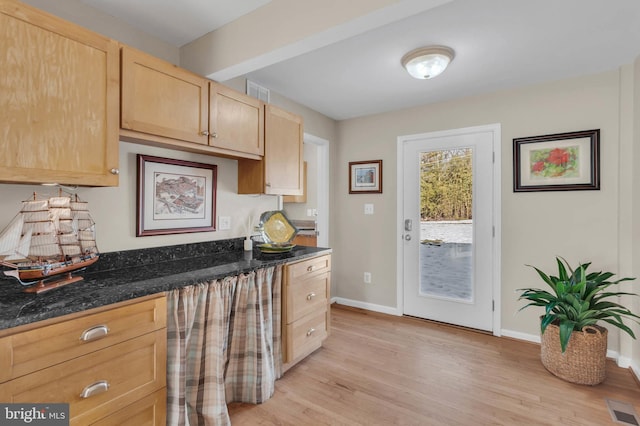 kitchen featuring light brown cabinetry, light hardwood / wood-style flooring, and dark stone countertops