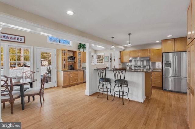 kitchen featuring hanging light fixtures, a kitchen breakfast bar, stainless steel appliances, light hardwood / wood-style floors, and kitchen peninsula