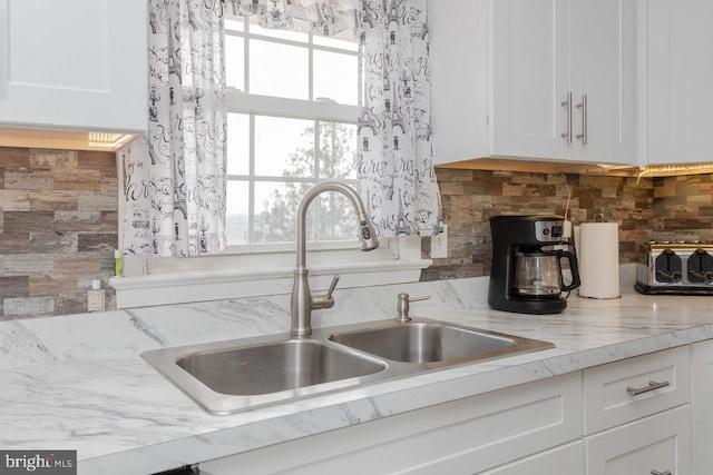 kitchen featuring backsplash, light stone countertops, white cabinetry, and sink