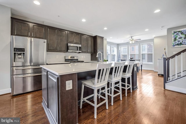 kitchen featuring backsplash, dark brown cabinets, an island with sink, and appliances with stainless steel finishes