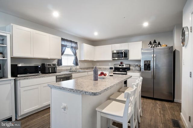 kitchen featuring stainless steel appliances, sink, white cabinetry, a kitchen island, and a breakfast bar area