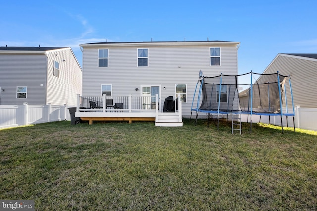 rear view of property with a lawn, a trampoline, and a wooden deck