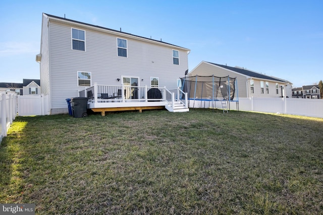 rear view of house with a lawn, a deck, and a trampoline