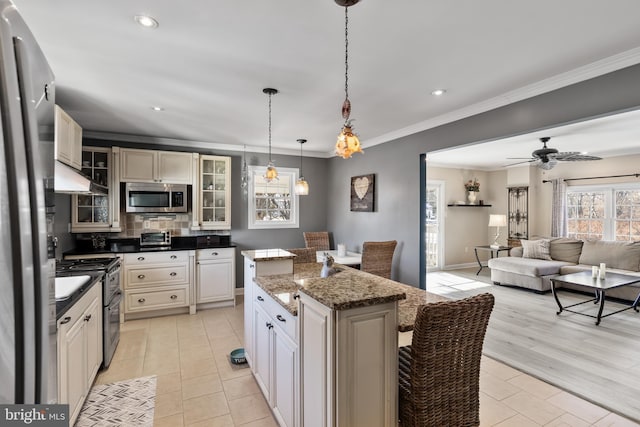 kitchen featuring appliances with stainless steel finishes, ceiling fan, dark stone countertops, a kitchen island, and hanging light fixtures