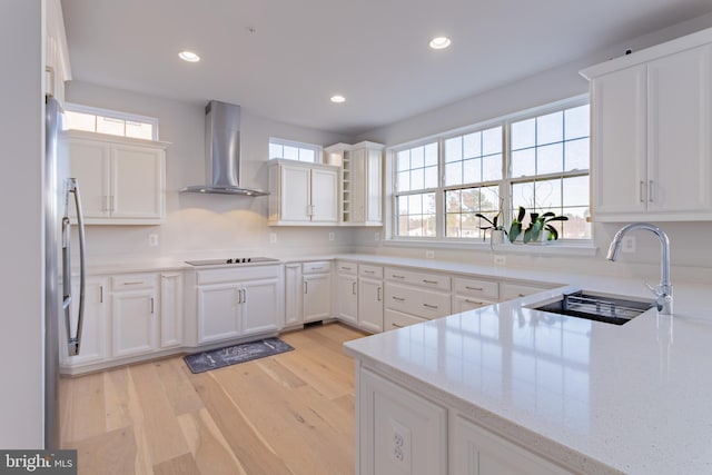 kitchen featuring white cabinets, black electric stovetop, wall chimney exhaust hood, light wood-type flooring, and light stone counters