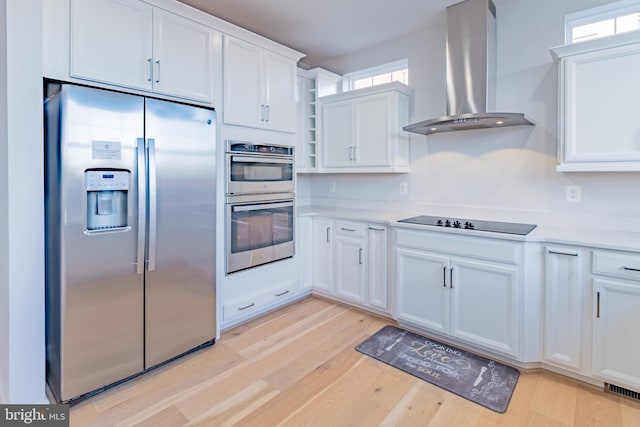 kitchen featuring white cabinets, wall chimney exhaust hood, stainless steel appliances, and light hardwood / wood-style flooring