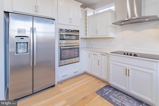 kitchen with wall chimney exhaust hood, white cabinetry, stainless steel appliances, and light hardwood / wood-style flooring