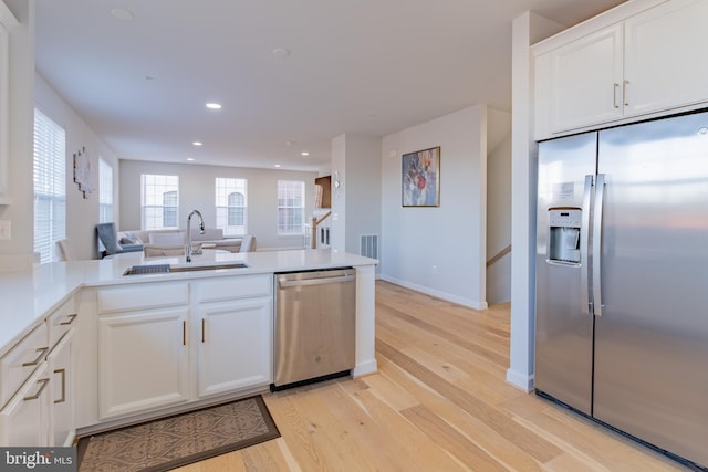 kitchen with kitchen peninsula, appliances with stainless steel finishes, light wood-type flooring, sink, and white cabinets