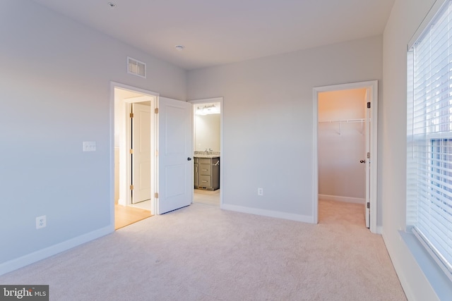 unfurnished bedroom featuring a spacious closet, a closet, and light colored carpet