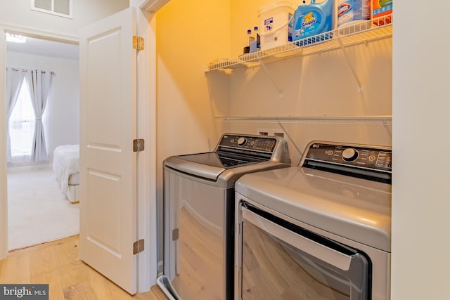 clothes washing area with washer and dryer and light wood-type flooring