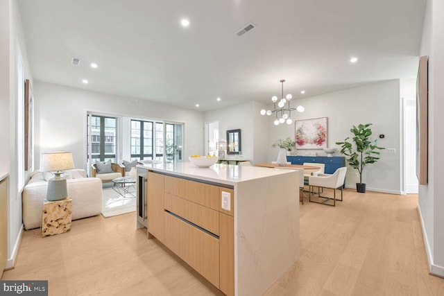 kitchen with pendant lighting, light hardwood / wood-style flooring, light brown cabinetry, a kitchen island, and a chandelier