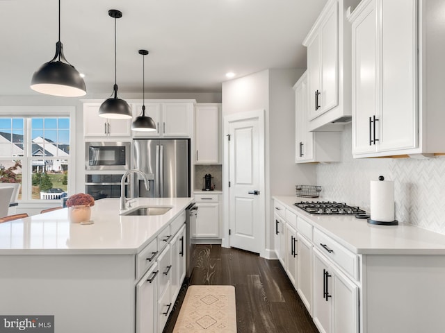 kitchen featuring white cabinetry, hanging light fixtures, stainless steel appliances, dark hardwood / wood-style flooring, and an island with sink