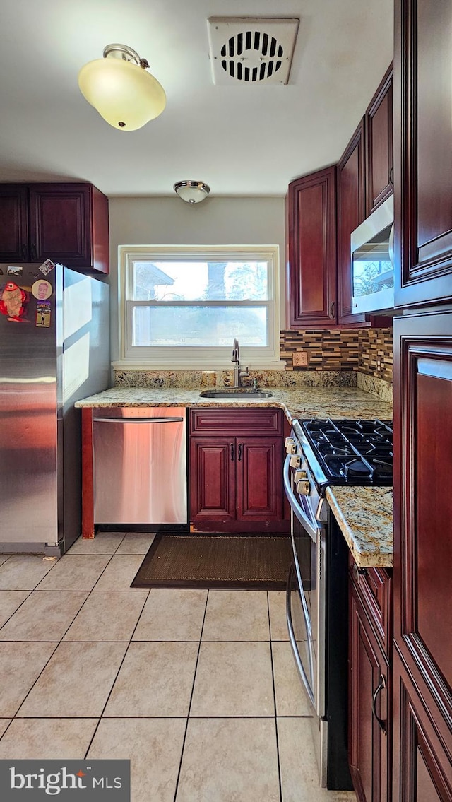 kitchen featuring light tile patterned flooring, appliances with stainless steel finishes, sink, decorative backsplash, and light stone counters