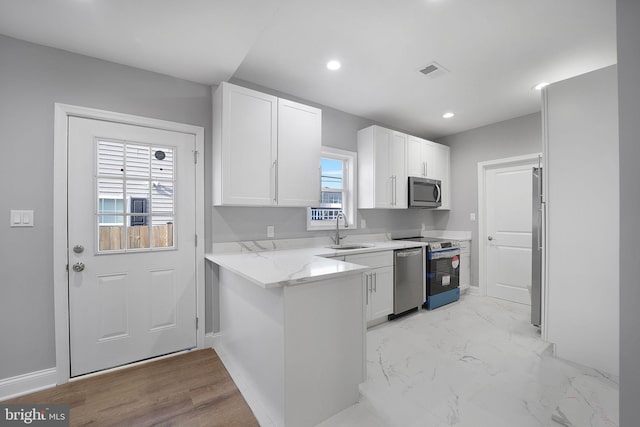 kitchen with white cabinets, sink, appliances with stainless steel finishes, light stone counters, and kitchen peninsula