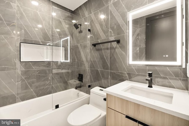 full bathroom with vanity, toilet, tiled shower / bath, and tile walls