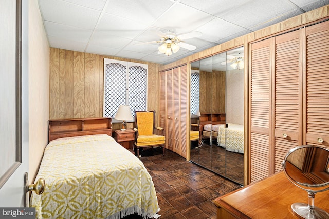 bedroom with a paneled ceiling, multiple closets, ceiling fan, and wood walls