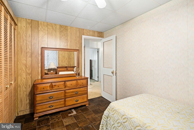 bedroom with a paneled ceiling, wooden walls, and a closet