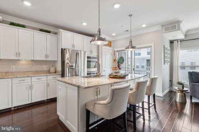 kitchen with white cabinets, stainless steel fridge, an island with sink, and hanging light fixtures