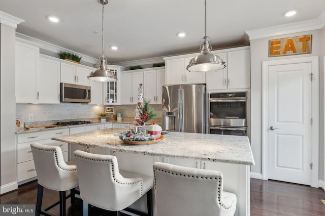 kitchen featuring white cabinetry, a kitchen island, decorative light fixtures, and appliances with stainless steel finishes