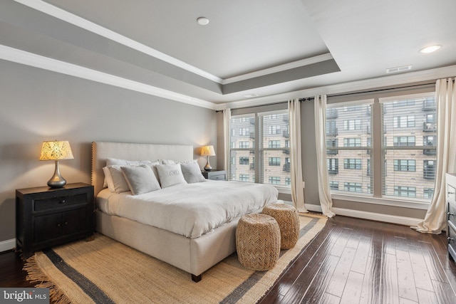 bedroom featuring dark wood-type flooring, a raised ceiling, multiple windows, and ornamental molding