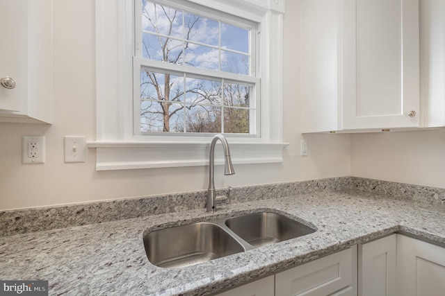 kitchen featuring light stone counters, sink, and white cabinets