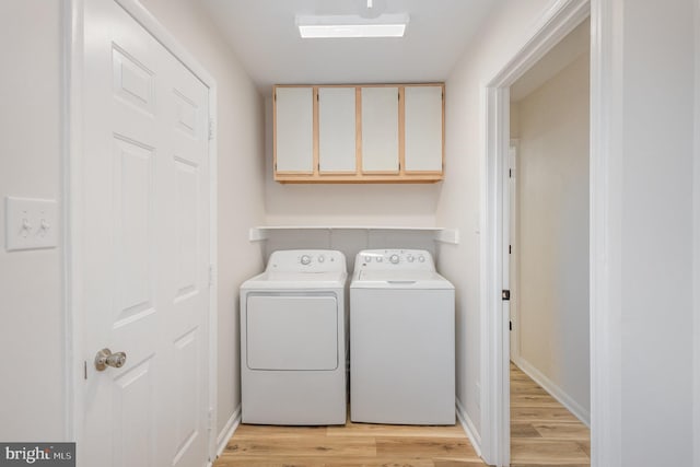 laundry room featuring washer and dryer, cabinets, and light wood-type flooring