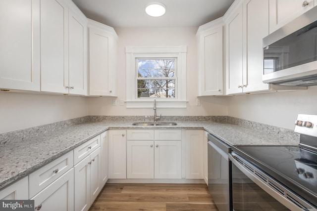 kitchen with light wood-type flooring, light stone counters, stainless steel appliances, sink, and white cabinets