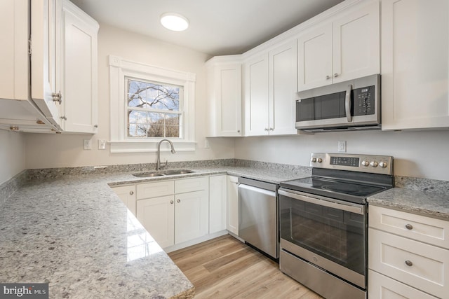 kitchen featuring white cabinets, stainless steel appliances, light stone counters, and sink