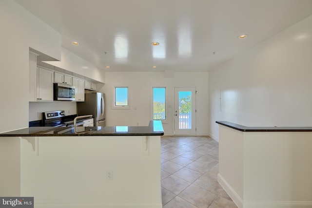 kitchen with a breakfast bar, white cabinets, appliances with stainless steel finishes, light tile patterned flooring, and kitchen peninsula